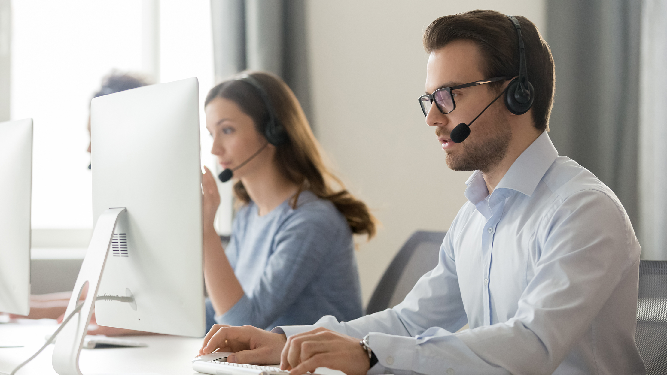 Diverse office workers wear headset with microphone browsing work on pc in coworking space, millennial male call center agent in glasses busy with computer consult client or customer online; Shutterstock ID 1419436334; purchase_order: -; job: -; client: -; other: -