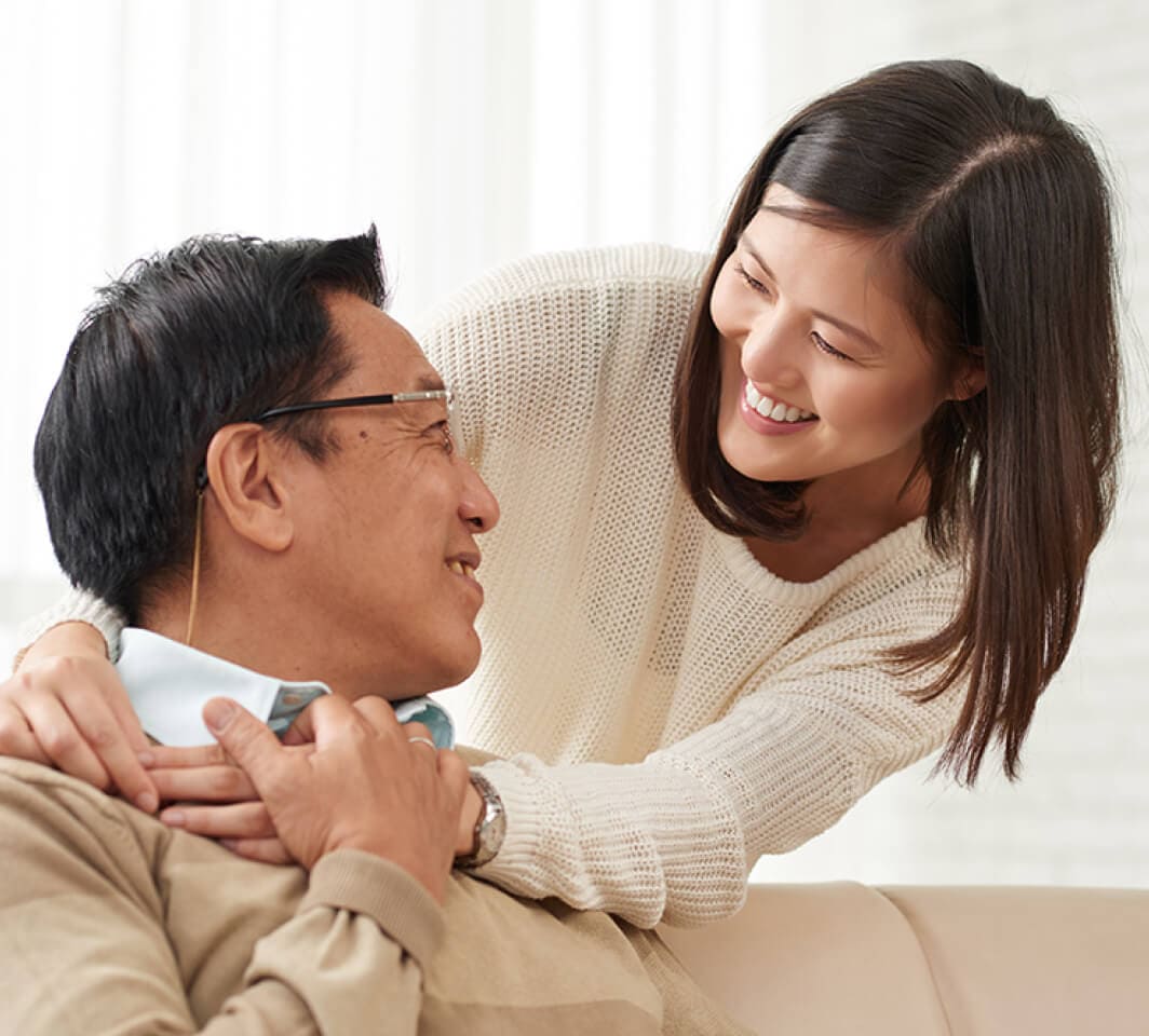 An elderly man smiling while being hugged by his smiling daughter 